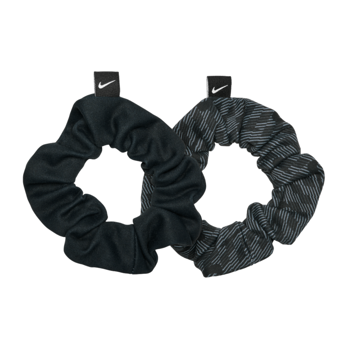 Two Nike hair scrunchies on a black background. One is solid black and the other has a dark grey patterned design. Both feature a small tag with a white swoosh logo.